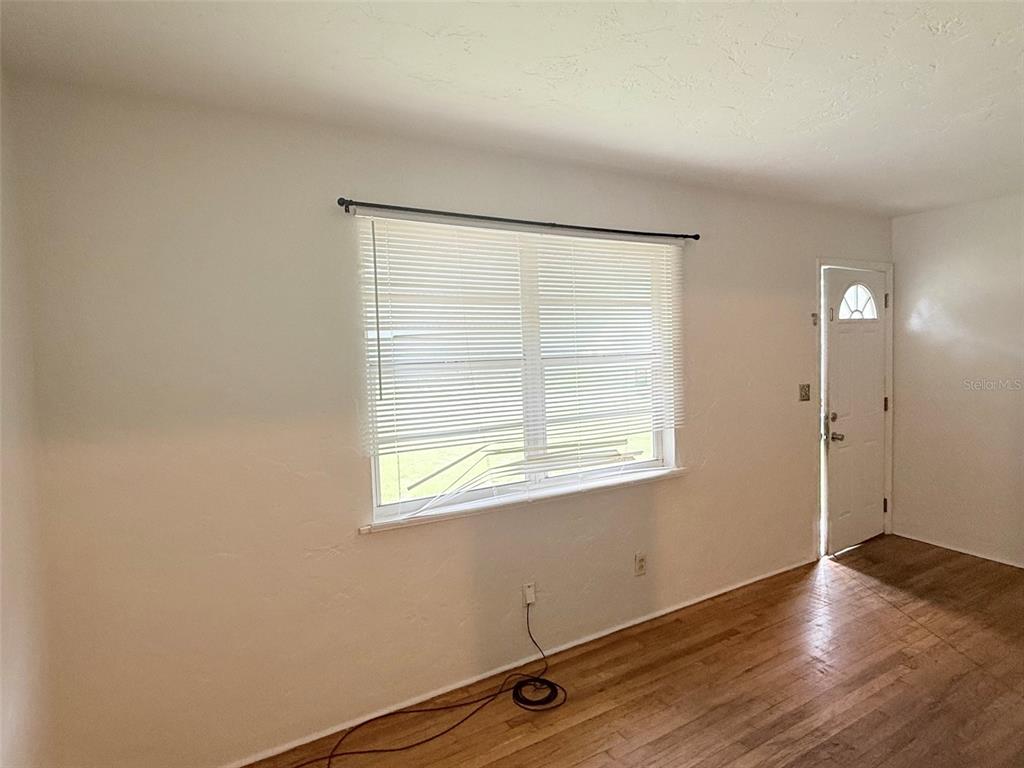 An empty room with hardwood floors, two windows with blinds, and a view into a kitchen — 5013 20TH STREET N, ST PETERSBURG, FL