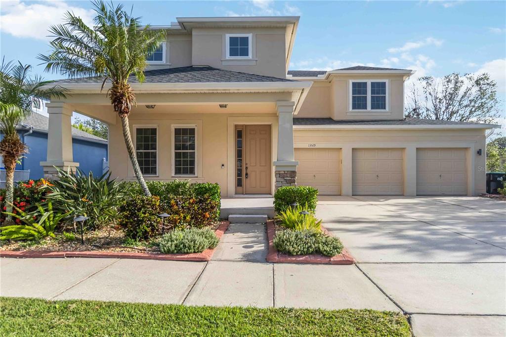 A two-story suburban house with a tan exterior, three-car garage, and a front porch — 13519 BICTON LANE, WINDERMERE, FL