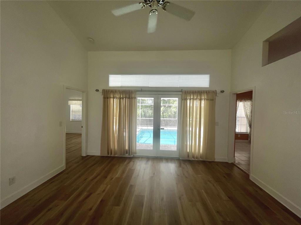 A living room with wood-look flooring, a ceiling fan, and glass doors overlooking a pool — 7116 PEBBLE BEACH LANE, SEMINOLE, FL