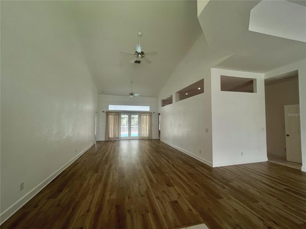 A spacious living area features high vaulted ceilings, light wood-look flooring, and glass sliding doors — 7116 PEBBLE BEACH LANE, SEMINOLE, FL
