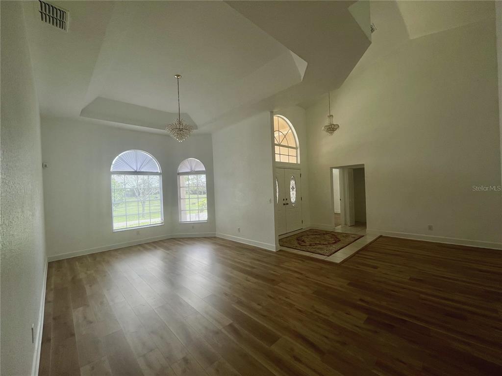 A bright, empty living room features high ceilings, wood-look flooring, and arched windows — 7116 PEBBLE BEACH LANE, SEMINOLE, FL