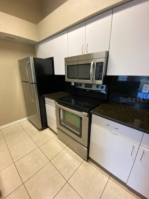 A kitchen features white cabinets, stainless steel appliances, and dark countertops over tiled floors — 5028 PARK CENTRAL DRIVE UNIT 2128, ORLANDO, FL