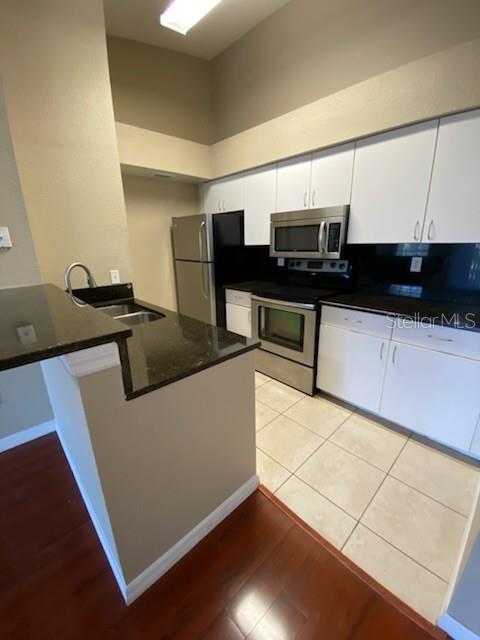 A kitchen features white cabinets, stainless steel appliances, dark countertops, and light-colored tile flooring — 5028 PARK CENTRAL DRIVE UNIT 2128, ORLANDO, FL