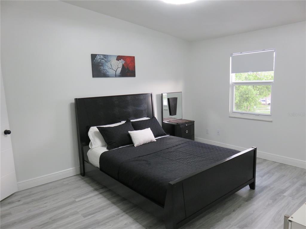 A bedroom features a black bed frame, light gray wood-look flooring, and white walls — 5401 SWEETWATER TERRACE CIRCLE UNIT 5401, TAMPA, FL