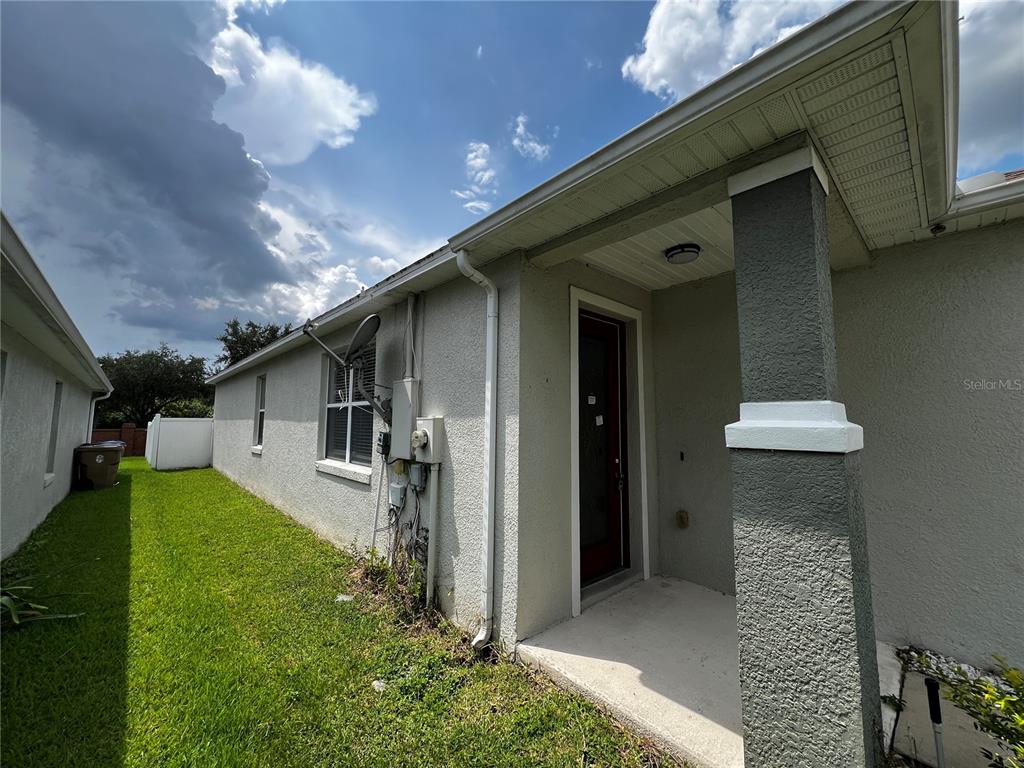 A side view of a house exterior featuring a covered entryway and a grassy yard — 454 JANICE KAY PLACE, KISSIMMEE, FL