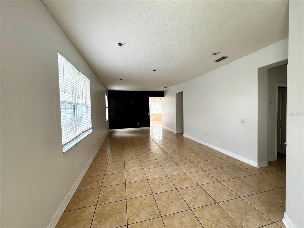 An empty room features beige tile flooring, white walls, a black accent wall, and recessed lighting — 454 JANICE KAY PLACE, KISSIMMEE, FL