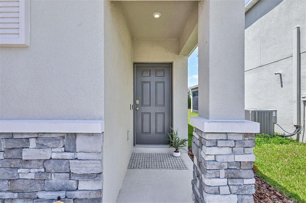 A gray front door is recessed within a covered entryway featuring stone-veneer columns — 6255 SPRINGMONT LOOP, PALMETTO, FL
