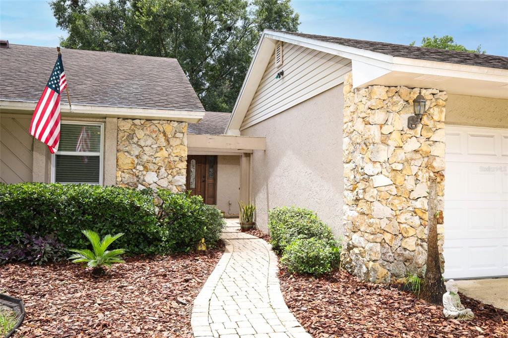 A stone-accented house exterior features a paved walkway leading to a recessed front entrance — 2450 CANTERCLUB TRAIL, APOPKA, FL