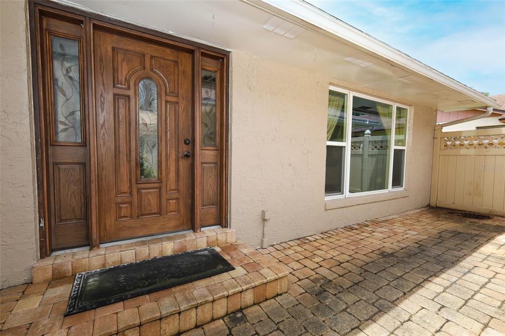 A wooden front door with sidelights sits beside a window on a paved patio area — 2450 CANTERCLUB TRAIL, APOPKA, FL