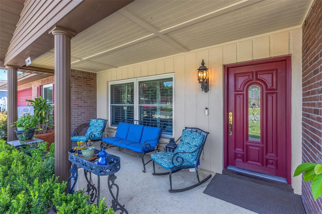 A covered front porch features a red door, blue patio furniture, and brick siding — 4001 HIGHGATE DRIVE, VALRICO, FL