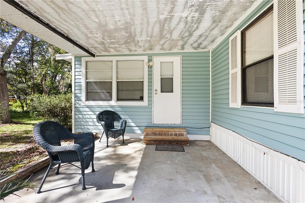 A covered concrete porch features light blue siding, a white door, and two wicker chairs — 11151 NW 112TH PLACE, CHIEFLAND, FL