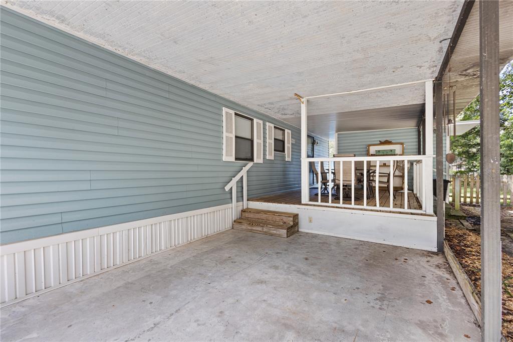 A concrete carport leads to a wooden deck with a white railing and blue siding — 11151 NW 112TH PLACE, CHIEFLAND, FL