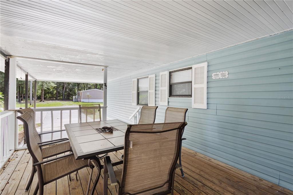 A covered wooden deck features a dining table with chairs against a light blue wall — 11151 NW 112TH PLACE, CHIEFLAND, FL