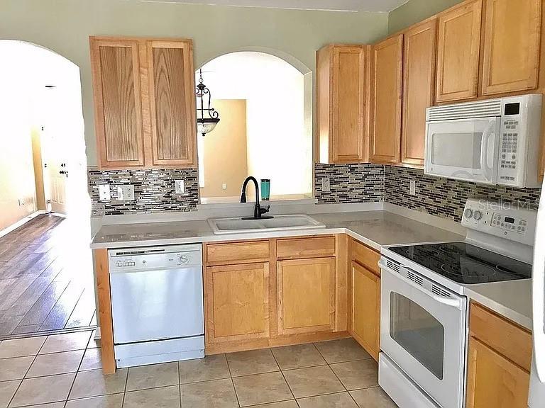 A kitchen features light wood cabinets, a tiled backsplash, and white appliances — 15647 STABLE RUN DRIVE, SPRING HILL, FL