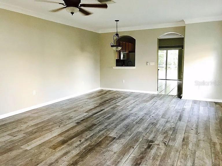 A living room features wood-look tile flooring, a ceiling fan, and a kitchen pass-through window — 15647 STABLE RUN DRIVE, SPRING HILL, FL