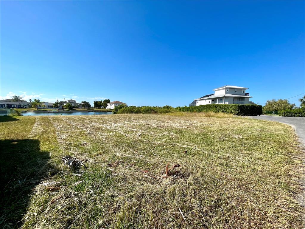 A vacant, grassy waterfront lot sits under a clear blue sky next to a house — 0 POINSETTIA DRIVE, HERNANDO BEACH, FL