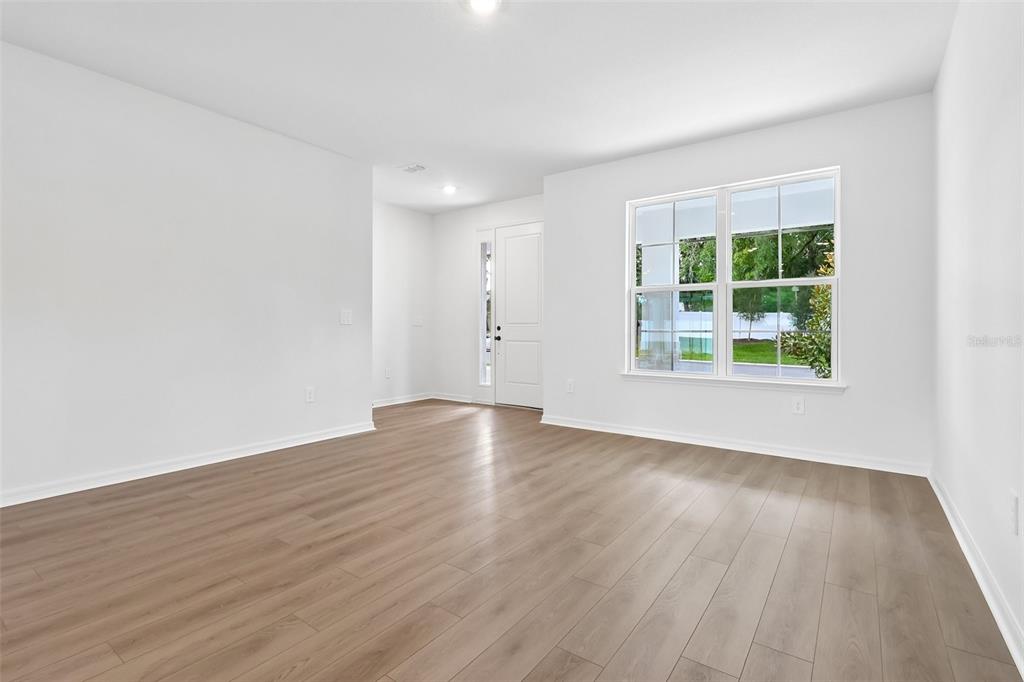 An empty room features light wood-look flooring, white walls, and a window facing the outdoors — 4272 DARBY COURT, EUSTIS, FL