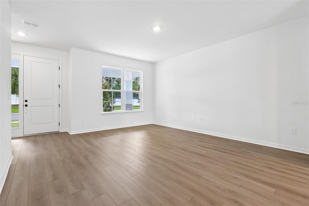 An empty room with white walls, light wood-look flooring, a window, and a white door — 4272 DARBY COURT, EUSTIS, FL