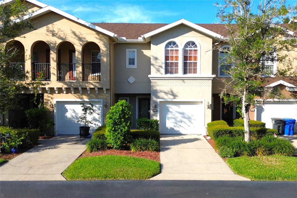 An exterior view of two attached townhomes with garages, arched balconies, and manicured landscaping — 314 SUMMER CLOUDS PL, BRANDON, FL