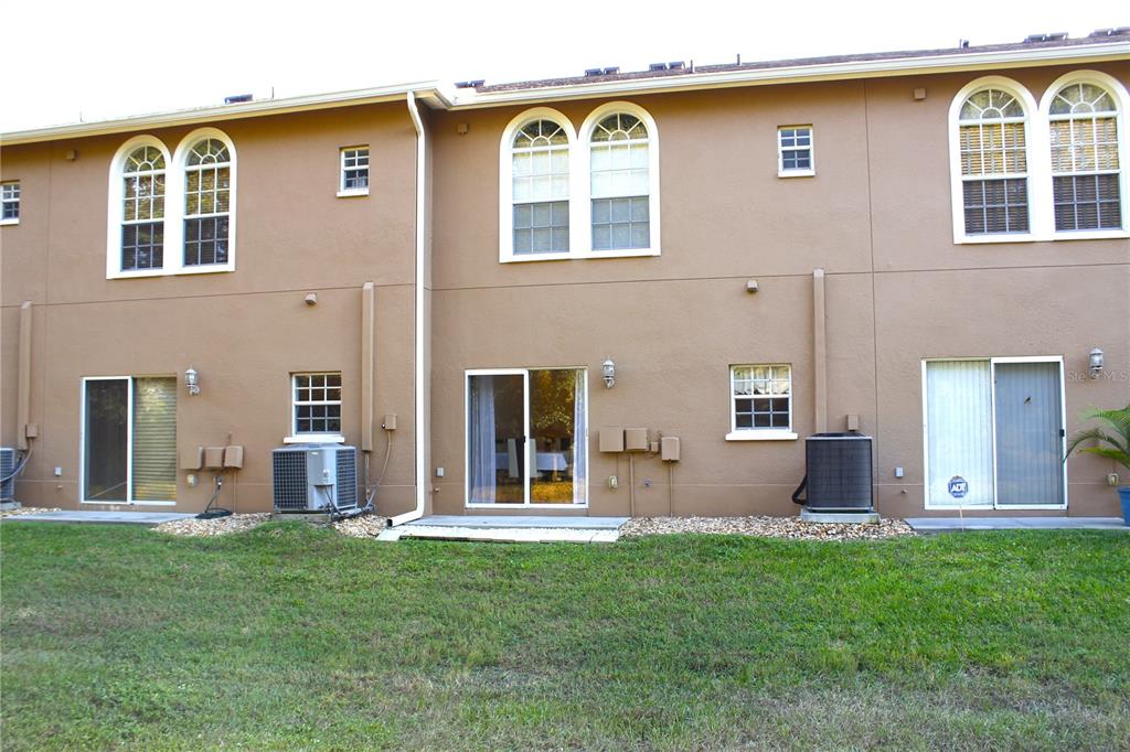 The exterior rear view of a two-story townhouse features stucco walls, sliding glass doors, and windows — 314 SUMMER CLOUDS PL, BRANDON, FL