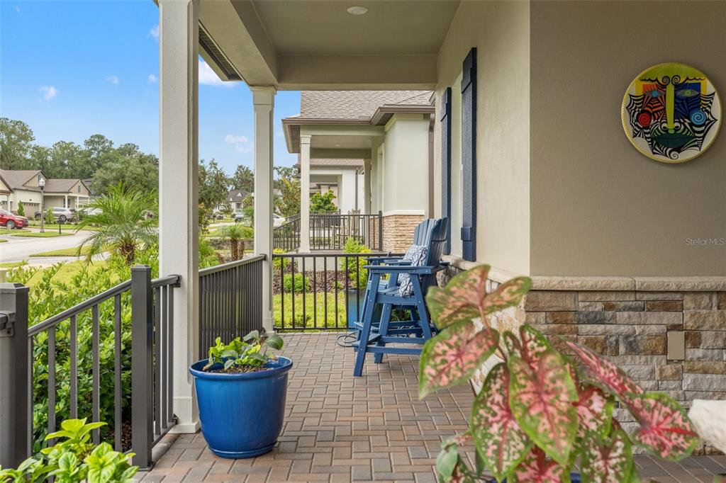 A covered brick porch features a blue chair, a potted plant, and stone wall accents — 5043 SOUTHERN VALLEY LOOP, BROOKSVILLE, FL