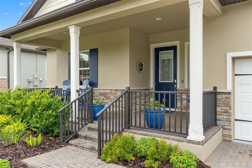 A covered front porch features a blue door, stone accents, and a metal railing — 5043 SOUTHERN VALLEY LOOP, BROOKSVILLE, FL