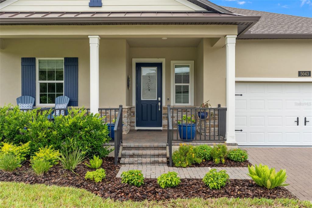 The exterior of a house features a covered porch, a blue front door, and landscaping — 5043 SOUTHERN VALLEY LOOP, BROOKSVILLE, FL
