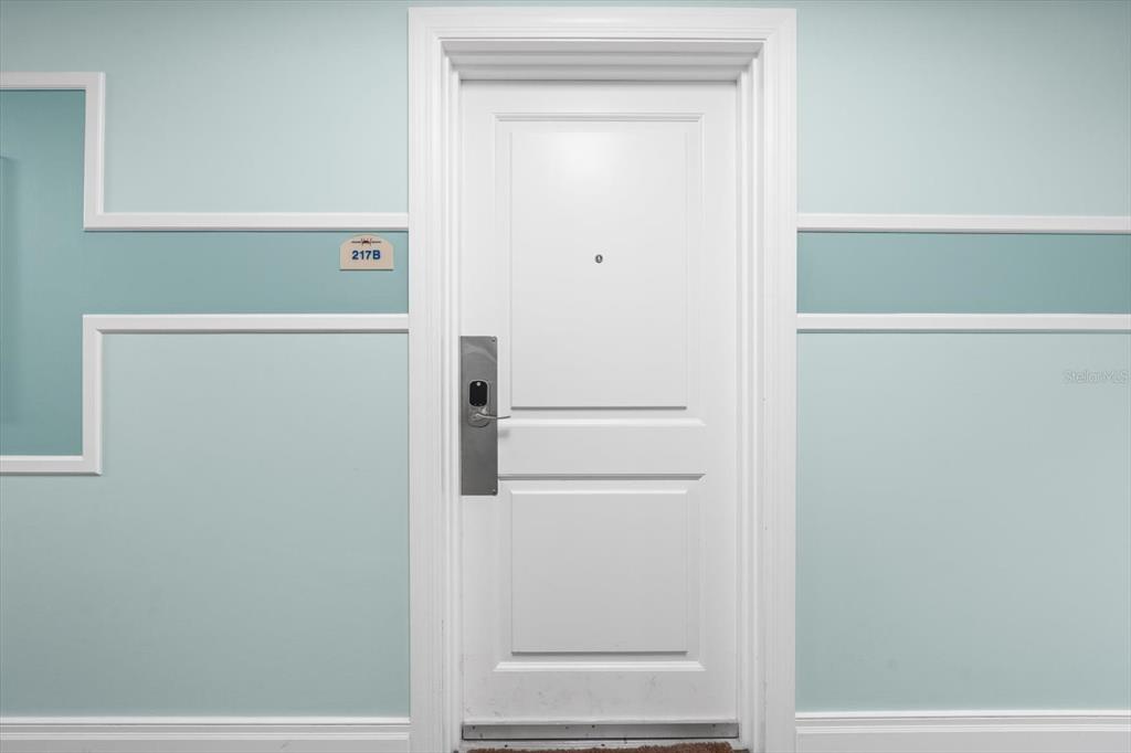 A white door with a keyless entry lock is centered on a light blue wall — 536 BAHIA BEACH BOULEVARD UNIT 320B, RUSKIN, FL
