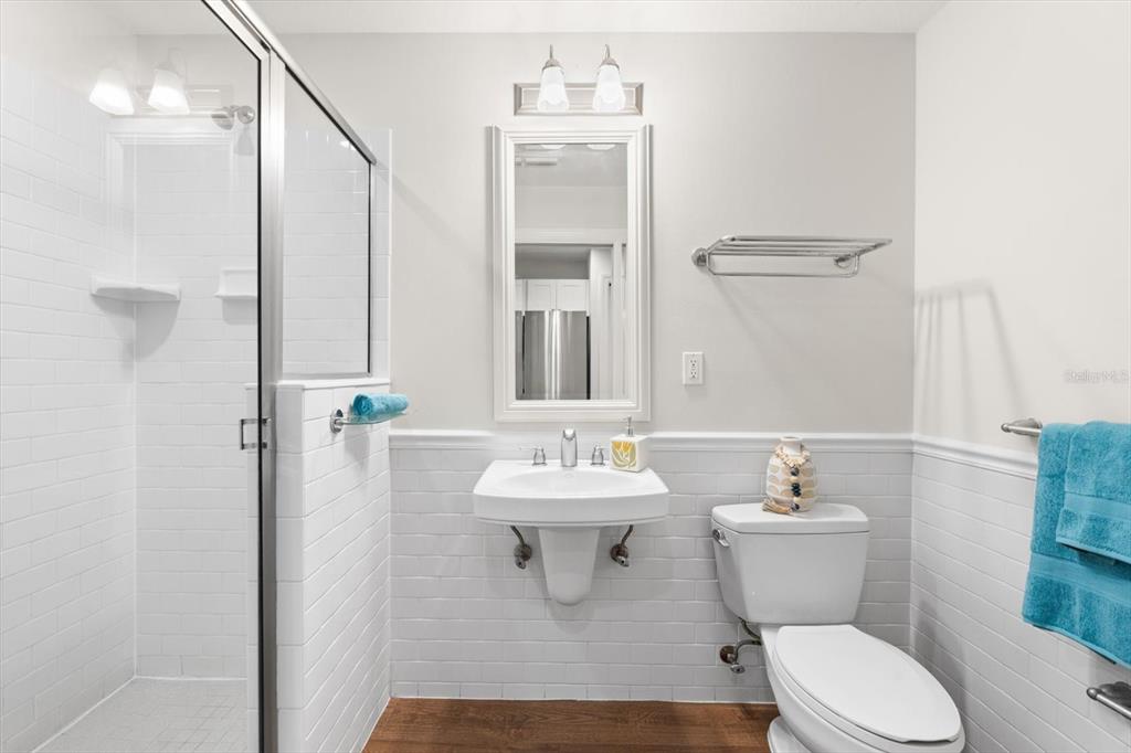 A bathroom features a wall-mounted sink, a glass-enclosed shower, and white subway tile wainscoting — 536 BAHIA BEACH BOULEVARD UNIT 320B, RUSKIN, FL