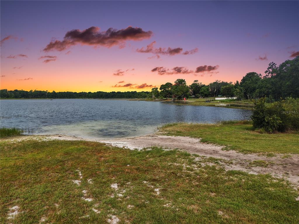 A grassy shoreline overlooks a calm lake under a colorful sunset sky — 17911 BEACH STREET, UMATILLA, FL