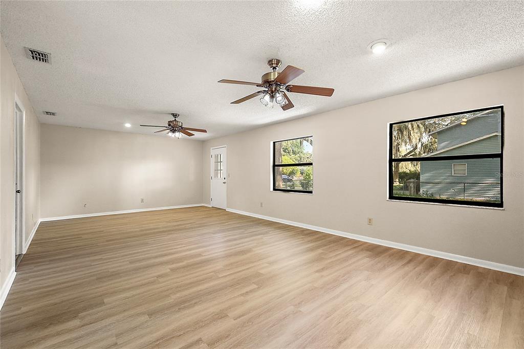 An empty room features light wood-look flooring, two ceiling fans, and two windows — 17911 BEACH STREET, UMATILLA, FL