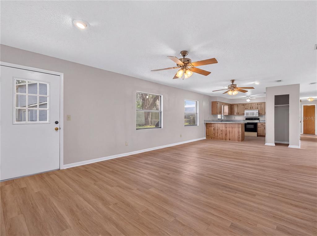An open-concept living area with wood-look flooring, two ceiling fans, and an adjacent kitchen — 17911 BEACH STREET, UMATILLA, FL