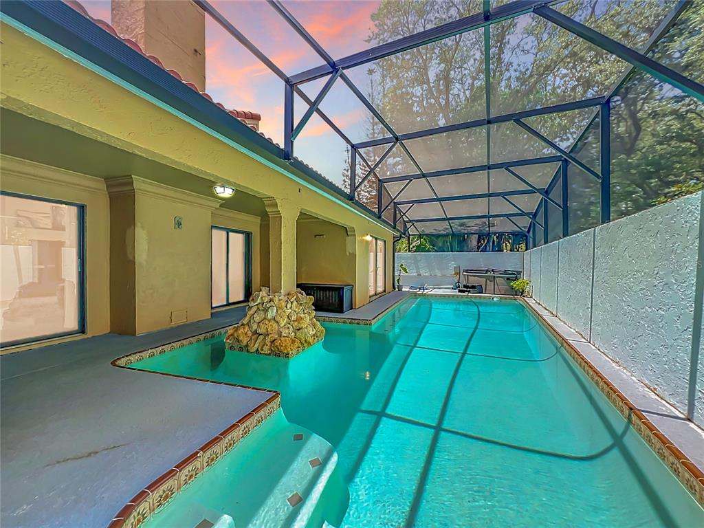 A screened-in swimming pool with a rock water feature sits beside a tan house exterior — 1162 E WINGED FOOT CIRCLE, WINTER SPRINGS, FL