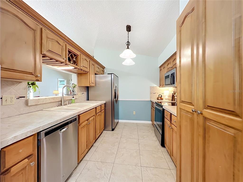 A galley kitchen features light wood cabinets, stainless steel appliances, and tile flooring — 1162 E WINGED FOOT CIRCLE, WINTER SPRINGS, FL