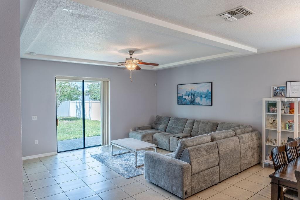 A living room with tile flooring, a large sectional sofa, and a sliding glass door — 612 SILVERTHORN PLACE, GROVELAND, FL