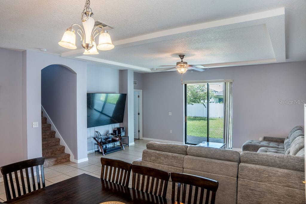 A living room with a tray ceiling, tile floors, a sectional sofa, and a television — 612 SILVERTHORN PLACE, GROVELAND, FL