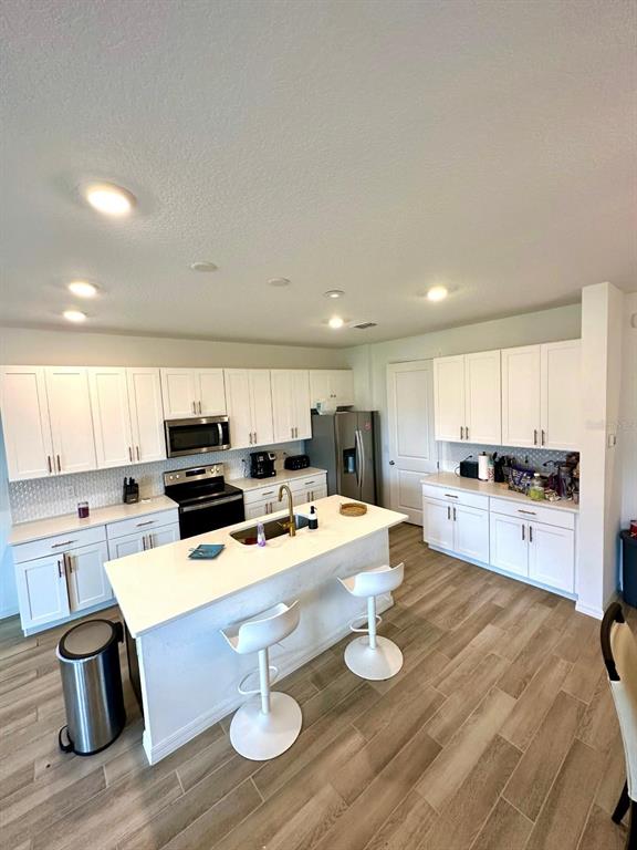 A modern kitchen features white cabinetry, a central island with bar stools, and wood-look flooring — 821 BENOI DR,, DAVENPORT, FL