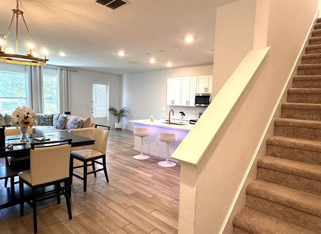 An open-concept kitchen and living area features light wood flooring and a carpeted staircase — 821 BENOI DR,, DAVENPORT, FL