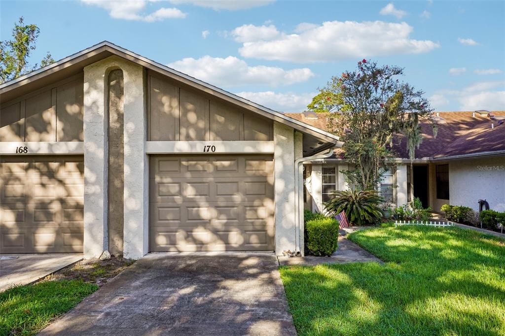 A tan-colored duplex exterior features two garage doors, a concrete driveway, and a grassy lawn — 170 HILL STREET, CASSELBERRY, FL