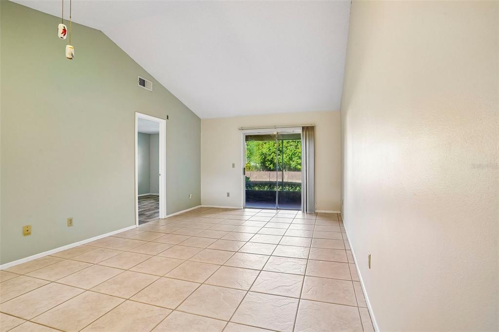 An empty living room features vaulted ceilings, beige tile flooring, and a sliding glass door — 170 HILL STREET, CASSELBERRY, FL