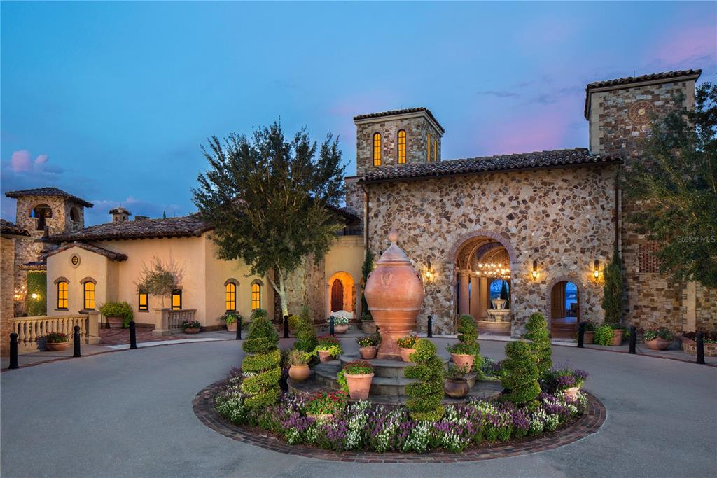 A stone-clad Mediterranean-style mansion features a circular driveway with a central fountain and landscaping — 16103 PENDIO DRIVE, MONTVERDE, FL