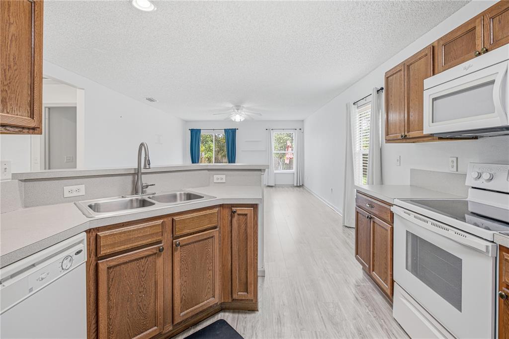 A kitchen with wood cabinets and white appliances overlooks an open-concept living area — 736 WYNFIELD CIRCLE, ST AUGUSTINE, FL