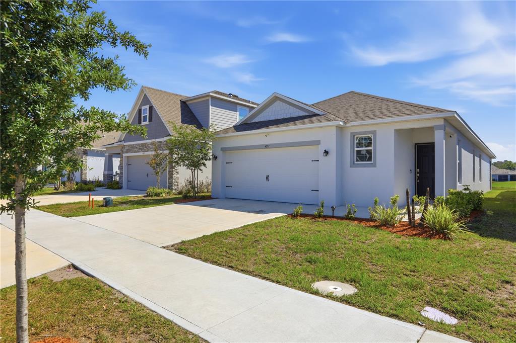 A single-story suburban house with a white stucco exterior, a two-car garage, and a sidewalk — 4057 SAGEFIELD DRIVE, HARMONY, FL