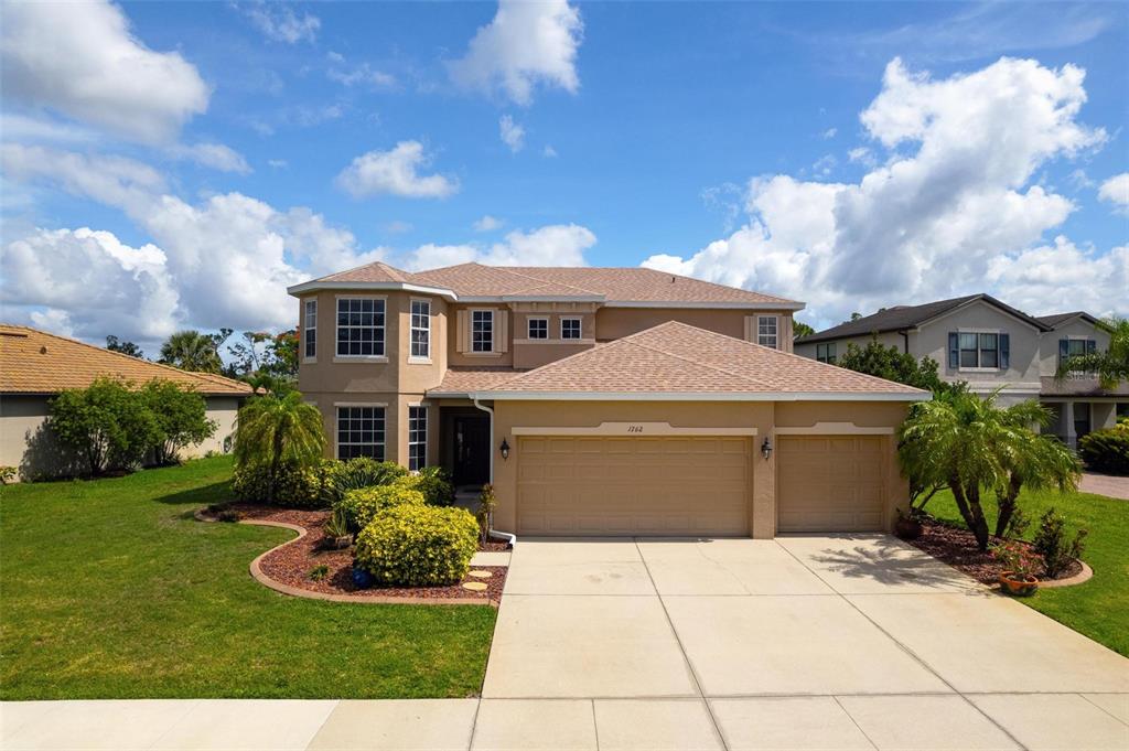 A two-story suburban house with a tan stucco exterior, a shingled roof, and a three-car garage — 1762 BOTTLEBRUSH WAY, NORTH PORT, FL