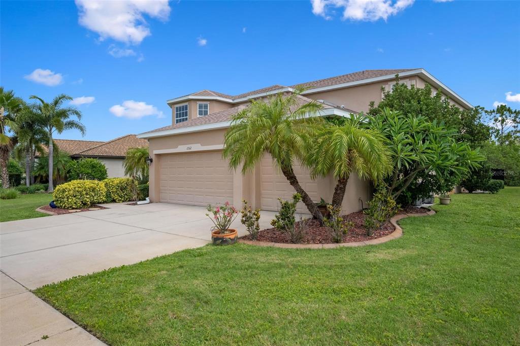 A two-story house with a beige exterior, a three-car garage, and palm trees in front — 1762 BOTTLEBRUSH WAY, NORTH PORT, FL