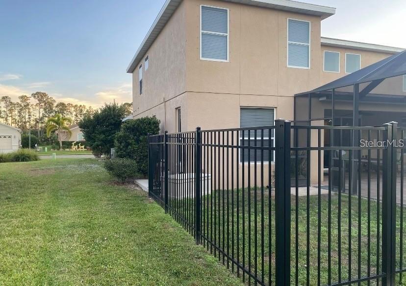 The exterior of a two-story tan house features a black metal fence and screened patio — 1762 BOTTLEBRUSH WAY, NORTH PORT, FL