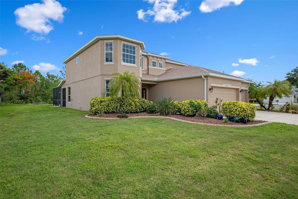 A two-story beige house with a garage and landscaped front yard under a blue sky — 1762 BOTTLEBRUSH WAY, NORTH PORT, FL