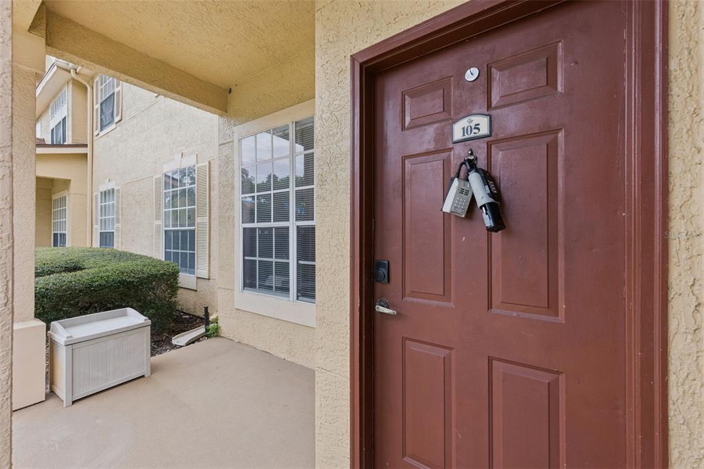 A brown front door with a lockbox hangs under a covered porch of a building — 832 GRAND REGENCY POINTE POINT UNIT 105, ALTAMONTE SPRINGS, FL