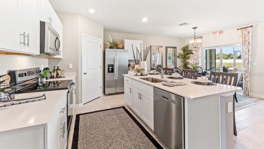 A modern kitchen features white cabinets, stainless steel appliances, a center island, and dining area — 9626 TURTLE GRASS CIRCLE, PUNTA GORDA, FL
