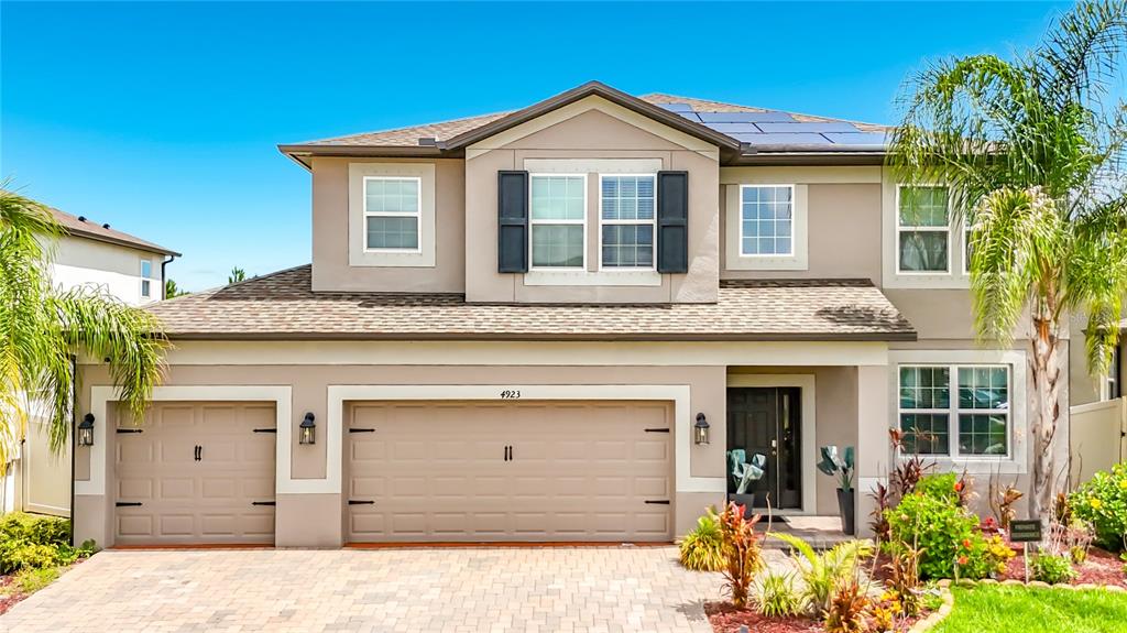 A two-story suburban house with a tan stucco exterior, a three-car garage, and solar panels — 4923 EAGLE ROCK DRIVE, WIMAUMA, FL